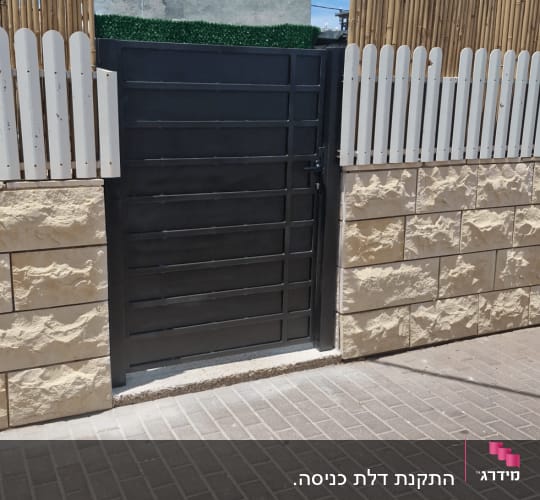 שער מתכת שחור בין גדרות עץ ואבן